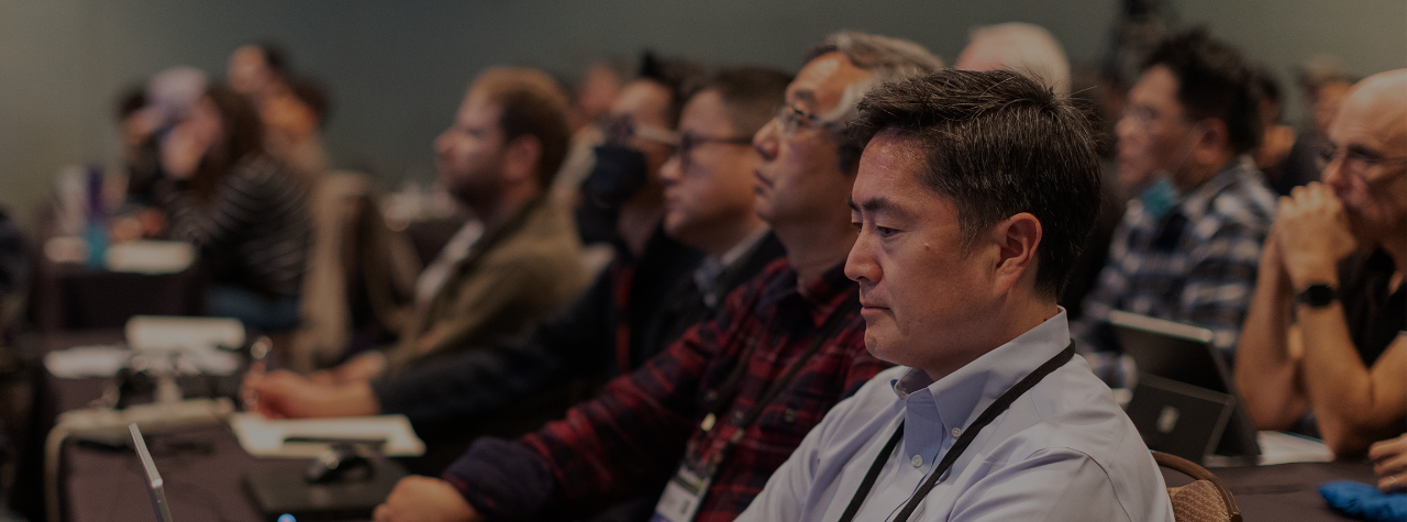 Man in audience takes notes during conference presentation.